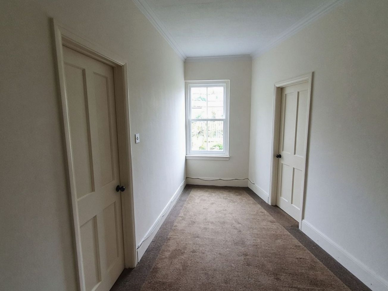 Hotel hallway, cream doors without numbers, brown runner, window at the end
