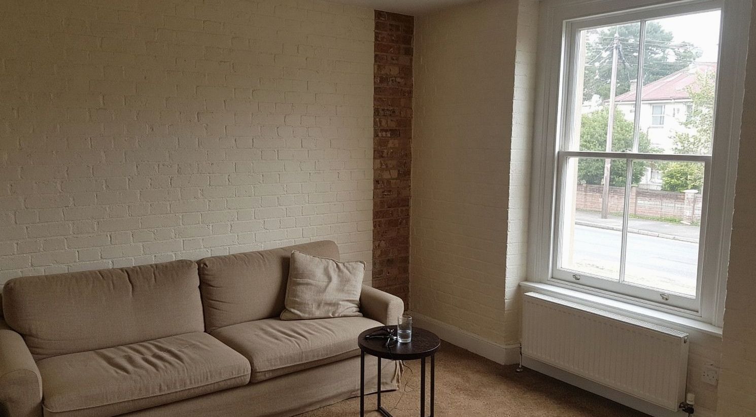 Sitting room with a cream sofa, painted brick and a street window